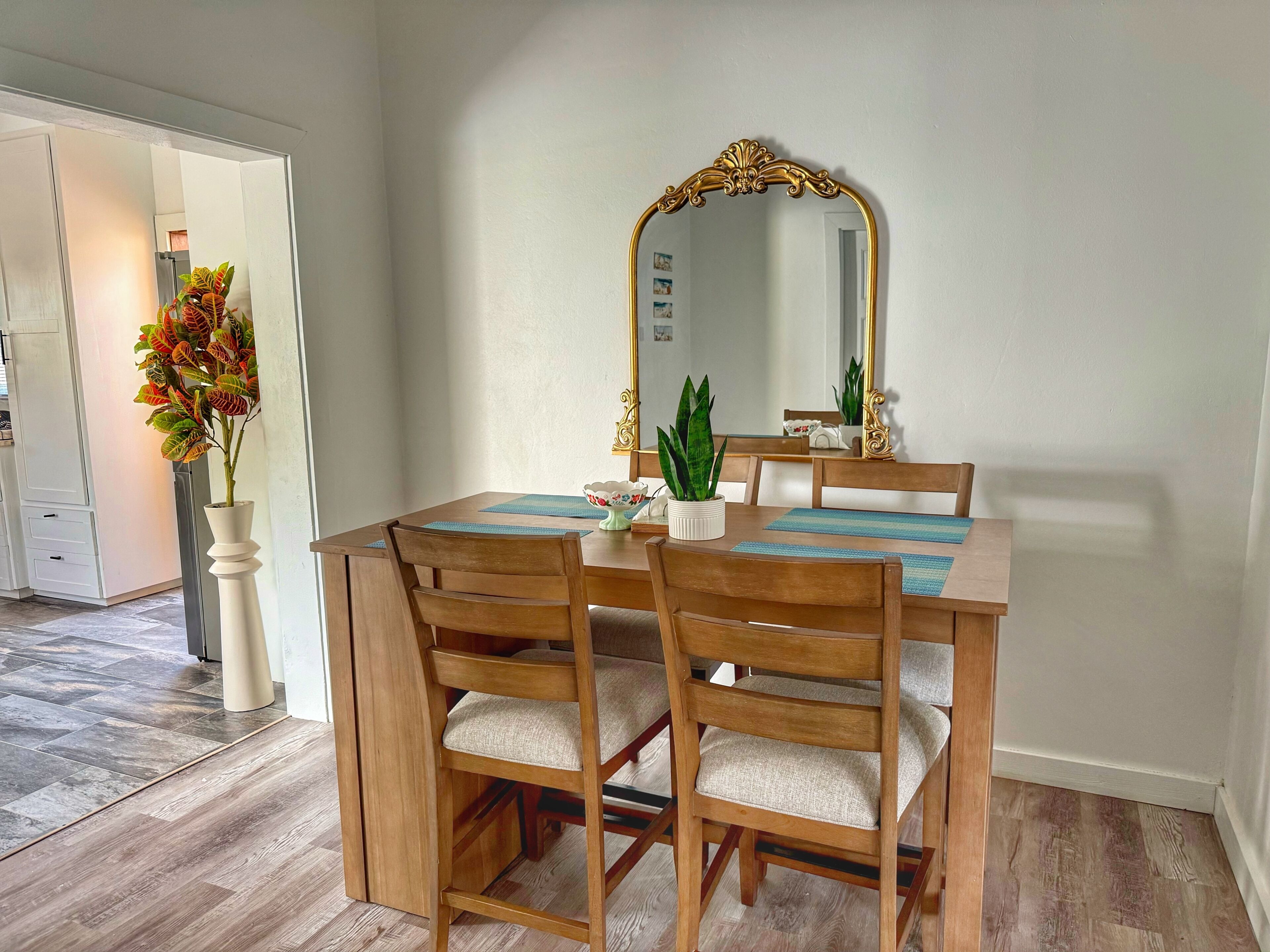 Un coin repas avec une table et des chaises en bois, un grand miroir décoratif et une plante en pot.