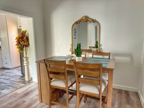 A dining area with a wooden table and chairs, a large ornate mirror, and a potted plant.