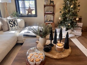 Een gezellige woonkamer met een kerstboom, een bank, een salontafel met lekkernijen en een boekenkast.