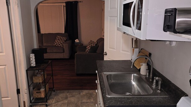 A compact kitchen with a gas stove, a microwave, and a sink. There is a small dining area with a couch and a ceiling fan.