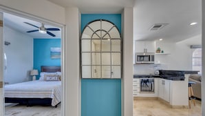 A modern bedroom with a bed, a ceiling fan, and a view into the adjacent kitchen. - Beachfront Escape at Mykonos Bay Resort 401B (San José del Cabo)
