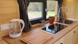 Angolo cottura funzionale con bollitore, tagliere, lavandino e finestra con tende.