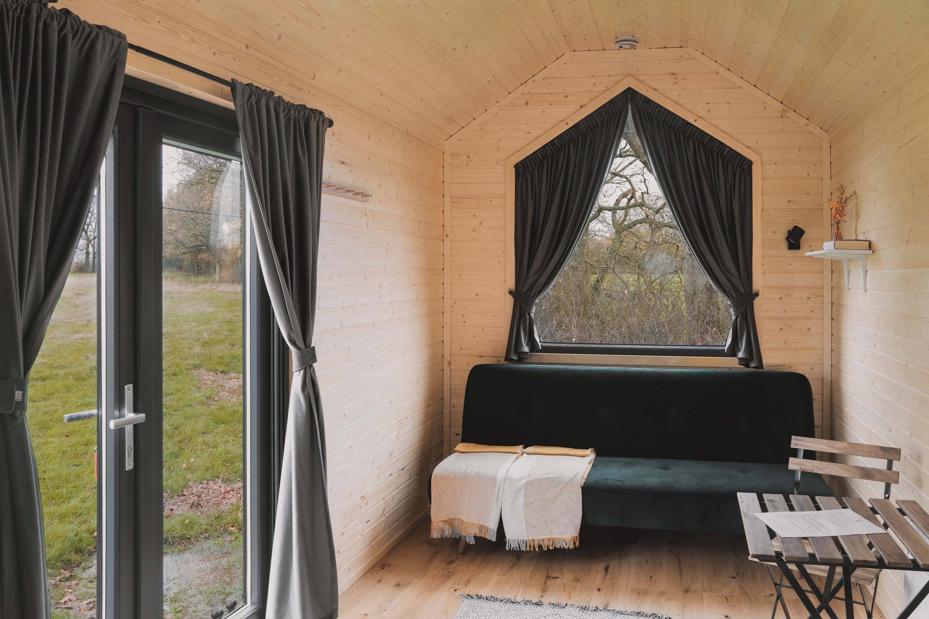 Interior acogedor de una cabaña con detalles de madera, un banco, una mesa y una ventana con cortinas.