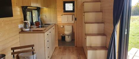A compact wooden cabin interior with a kitchenette, a toilet, and a window with curtains.