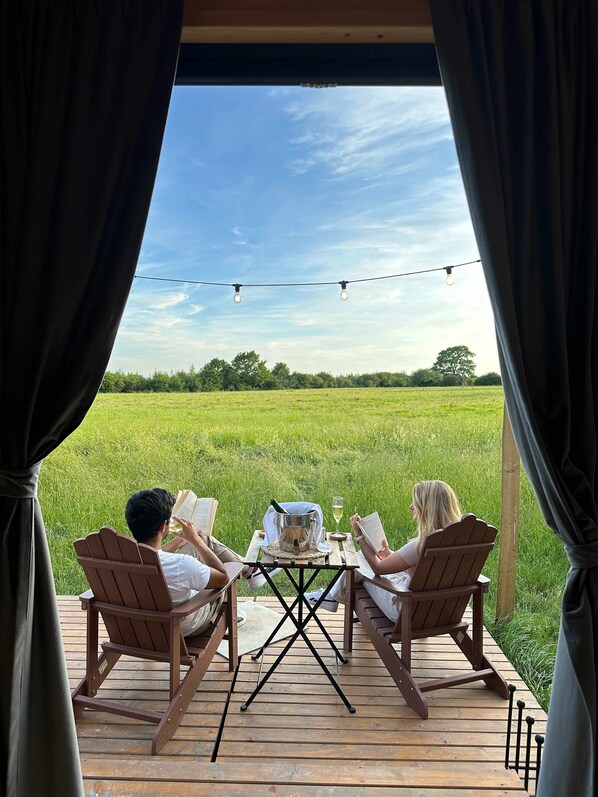 A wooden deck with a table and chairs, overlooking a green field. - The Field View 2 by Tiny Away (Egerton)