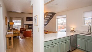 Una cocina moderna con armarios verdes, un comedor con mesa y sillas de madera, y una sala de estar con chimenea.