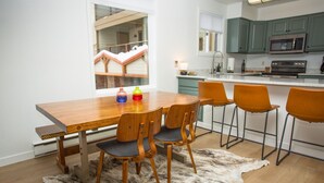 Una cocina moderna con una mesa de comedor de madera, cuatro sillas, una isla de cocina con taburetes altos y vistas a un balcón con una casa.