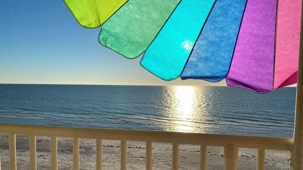 Une vue sur la plage avec une rambarde et des parasols colorés.