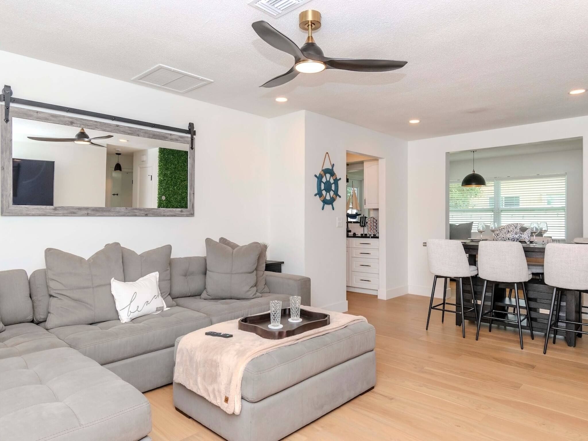 A modern living room with a sectional sofa, a coffee table, a ceiling fan, and a view into the kitchen.