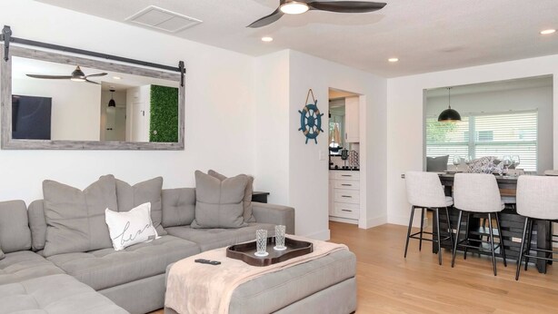 Un salon moderne avec un canapé d’angle, une table basse, un ventilateur de plafond et une vue sur la cuisine.