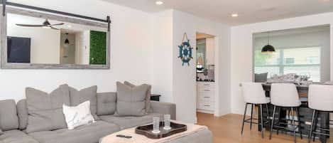 A modern living room with a sectional sofa, a coffee table, a ceiling fan, and a view into the kitchen.
