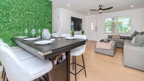 Un espace de vie moderne comprenant un coin repas, un canapé gris et un mur vert.
