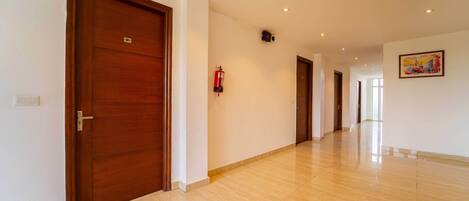 A hallway with wooden doors, a fire extinguisher, and a painting on the wall.