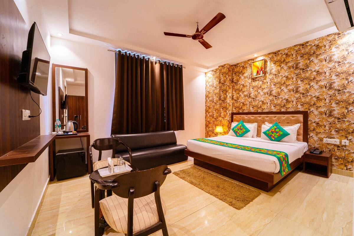A hotel room with a bed, a desk, a chair, a ceiling fan, and a TV.
