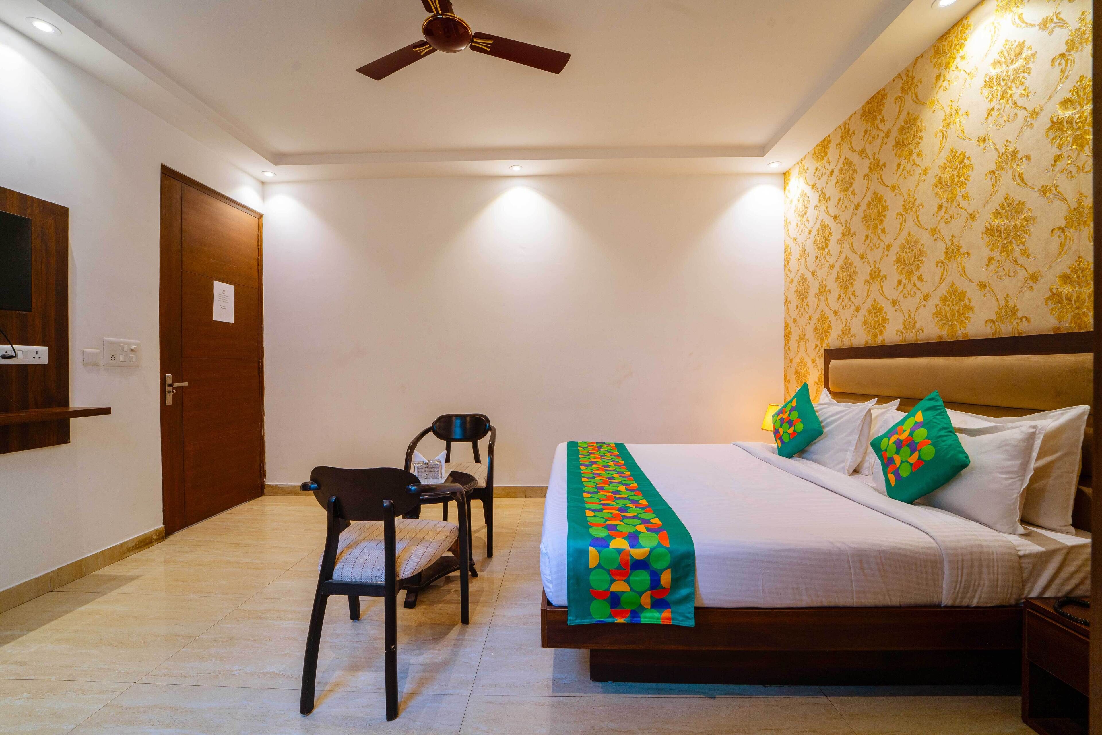 Habitación de hotel con cama, escritorio, silla, ventilador de techo y pared con diseño.