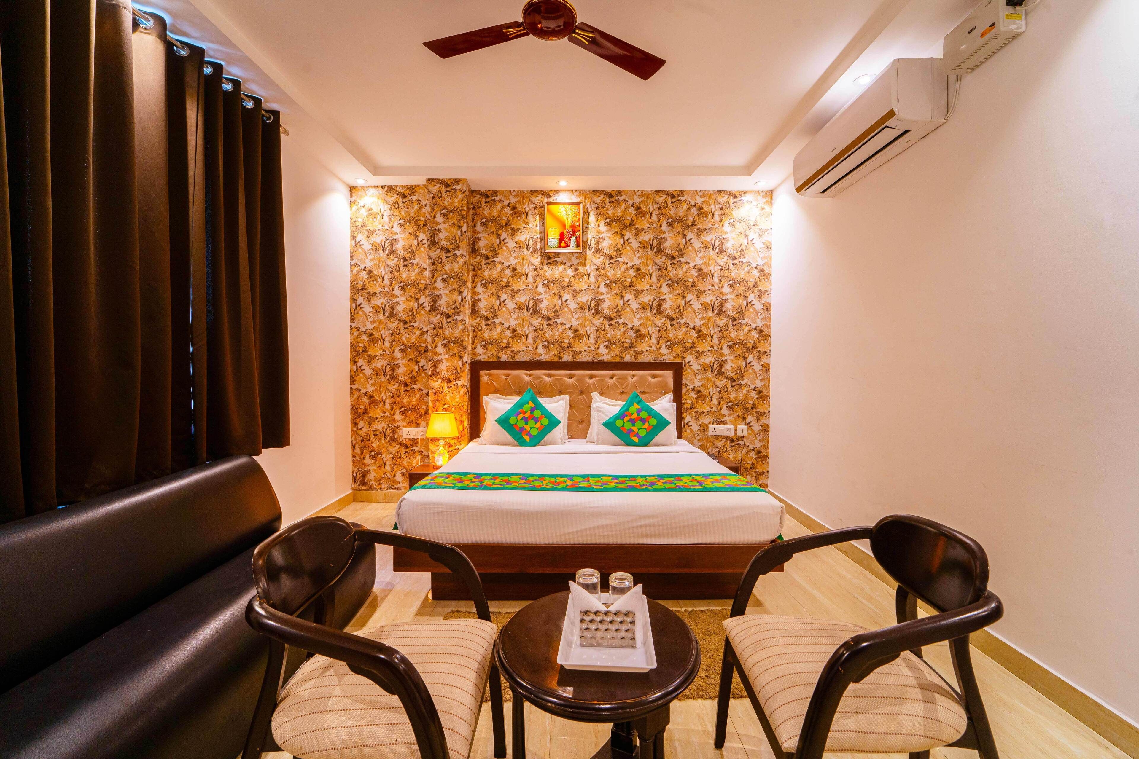 A hotel room with a bed, a ceiling fan, a table with two chairs, and a wall-mounted air conditioner.