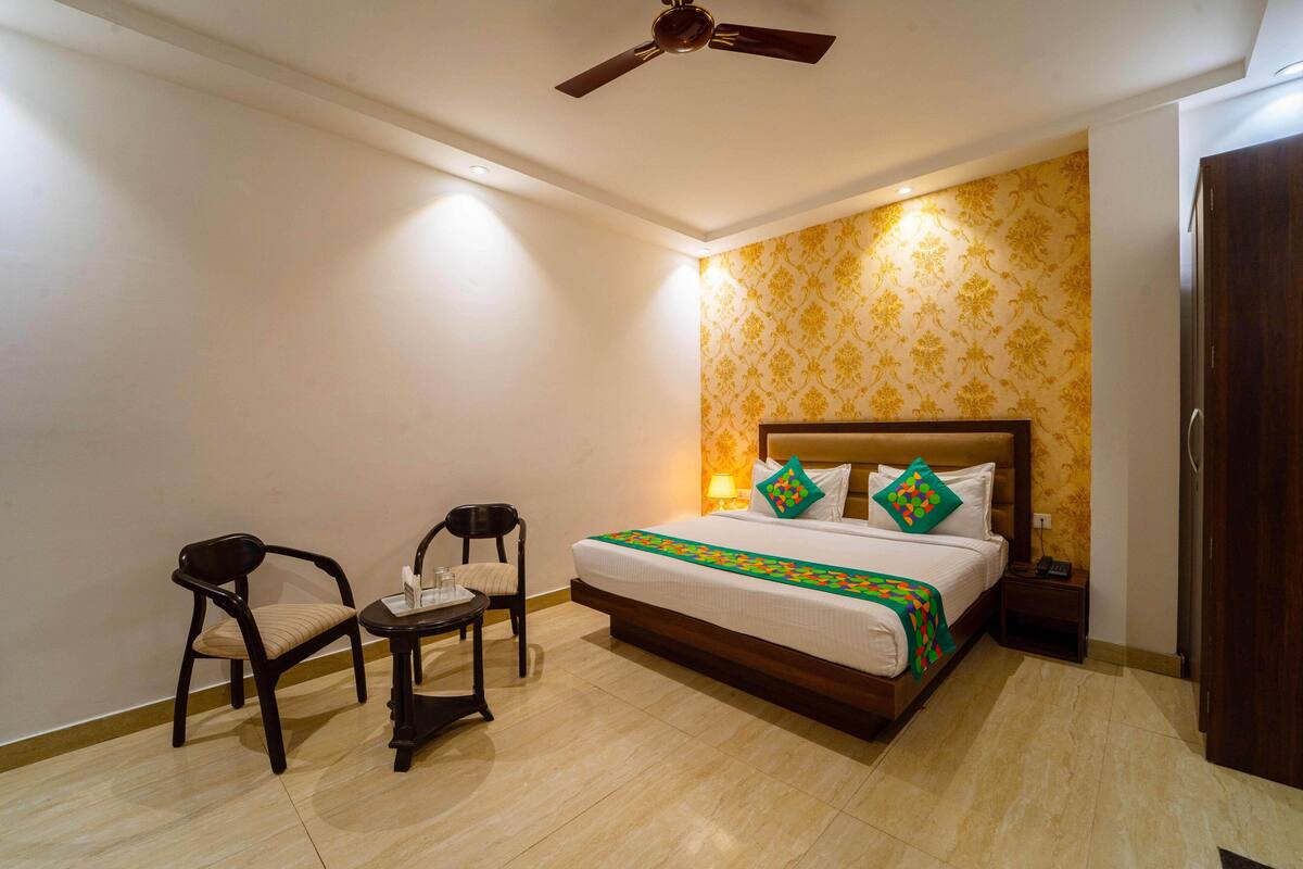 A hotel room with a bed, two chairs, a small table, a nightstand, and a ceiling fan.