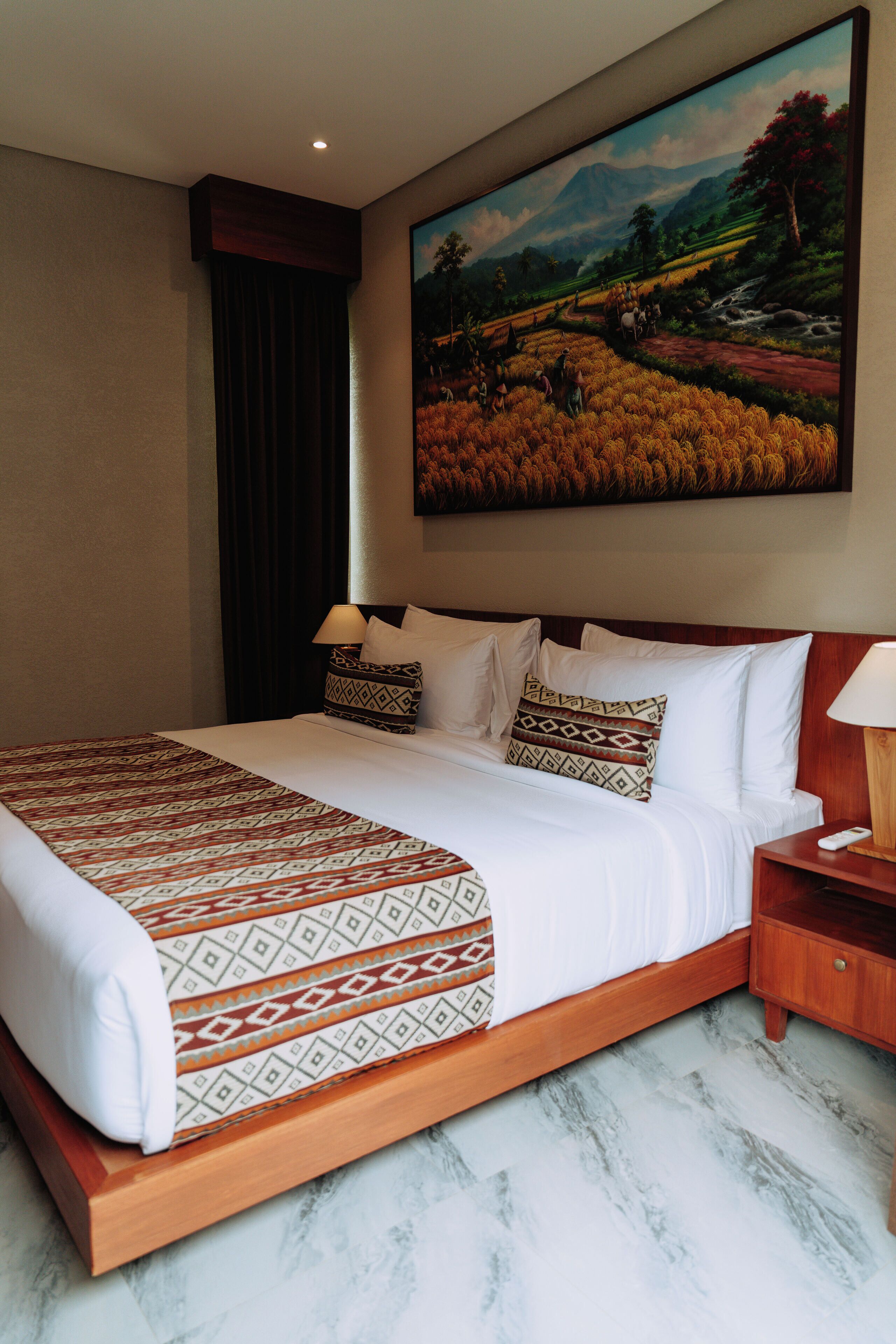 A hotel room with a large bed, a nightstand, a painting on the wall, and a window with curtains.