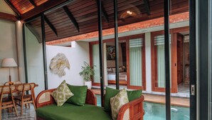 A room with a green sofa, wooden furniture, a large window, and a view of a pool. - Unagi Mas Villas by Emana (Mas)