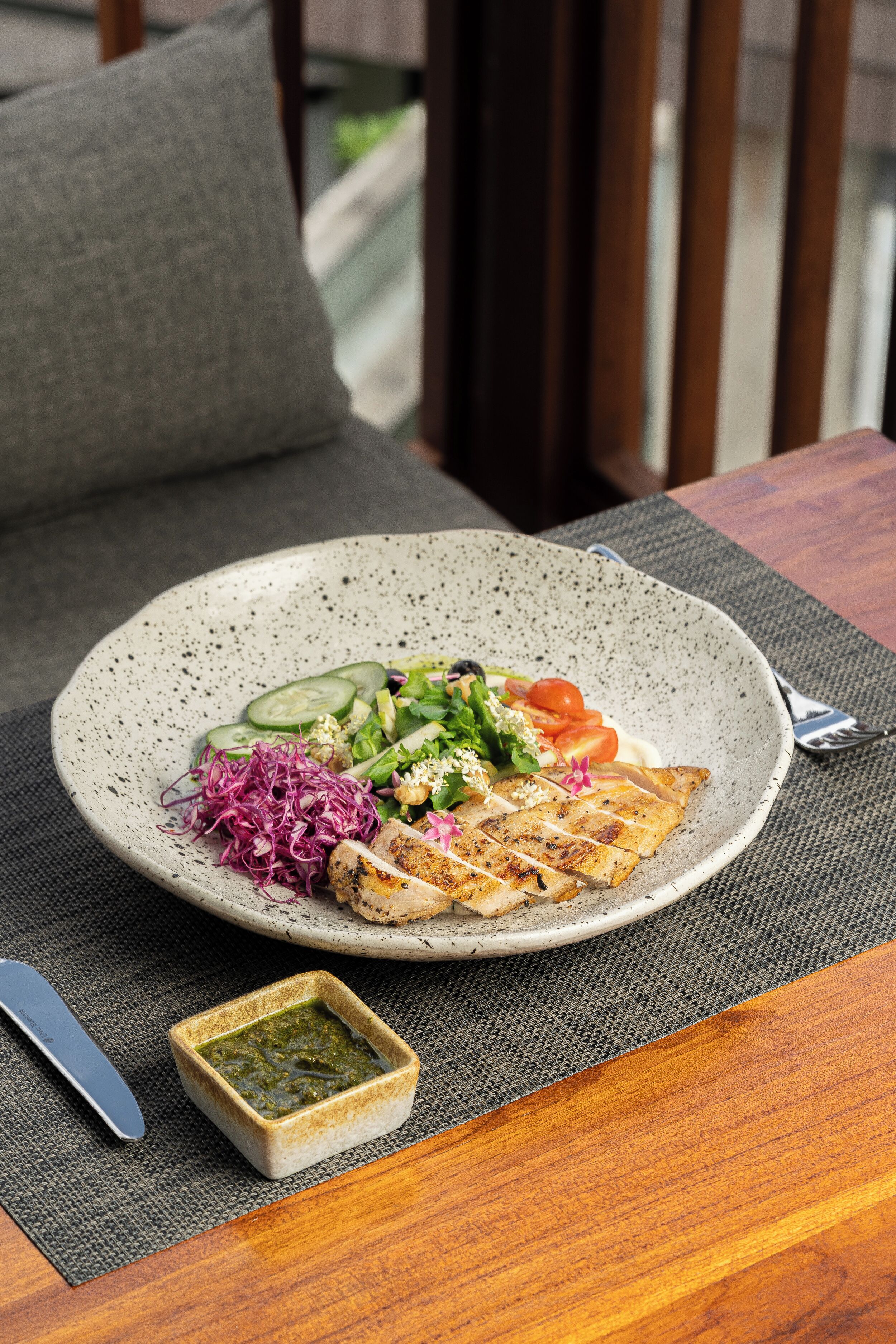 A plate of food on a table with a small bowl of sauce and a knife.