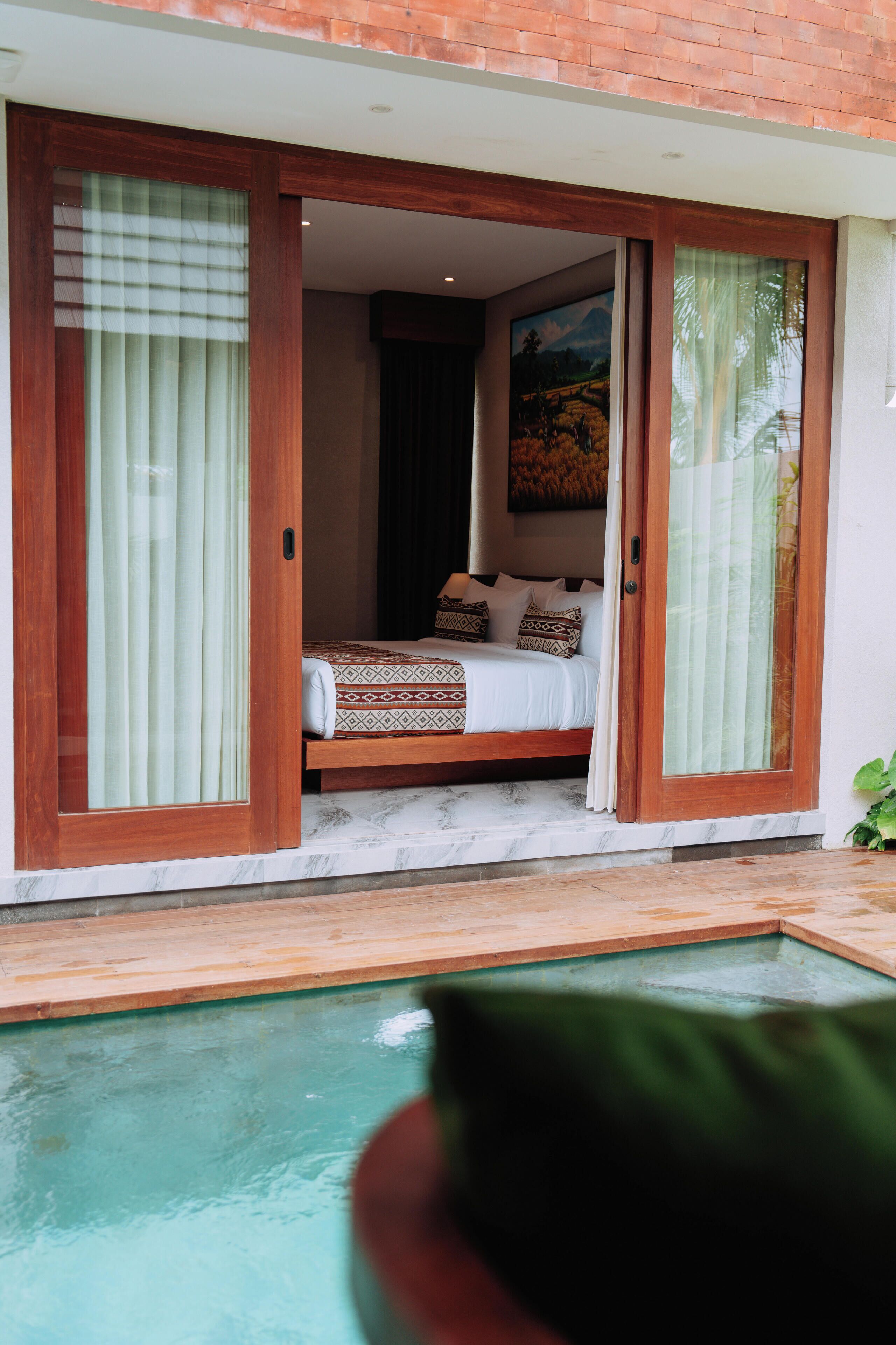Un dormitorio con cama, un cuadro y un ventanal corredero que da a una zona de piscina.