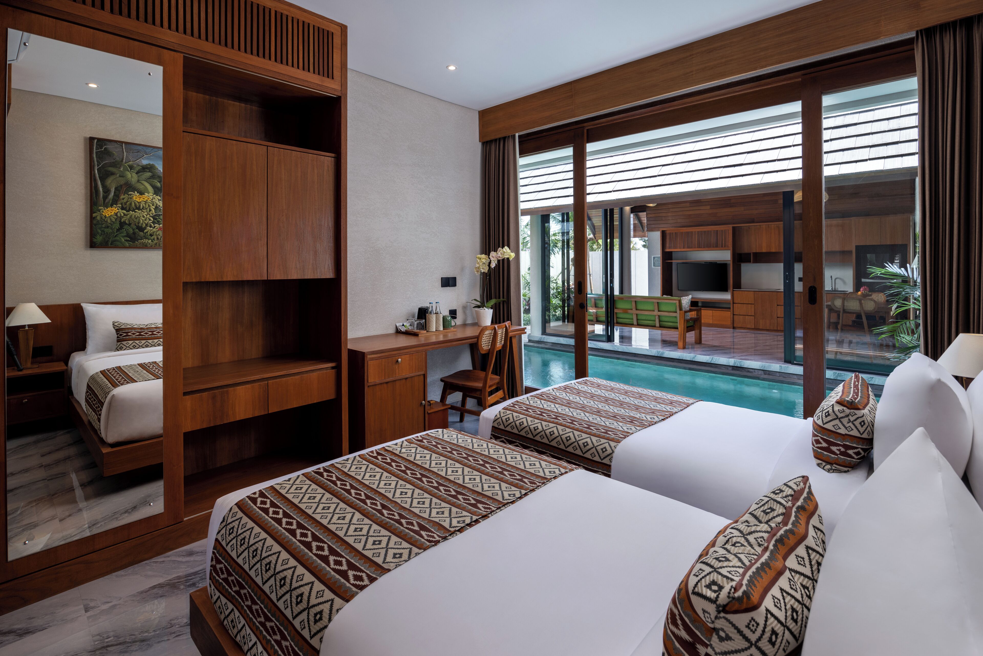 A hotel room with two beds, a desk, a chair, and a view of a swimming pool.