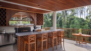 A modern outdoor kitchen with a bar area, wooden stools, and a view of lush greenery. - Unagi Mas Villas by Emana (Mas)