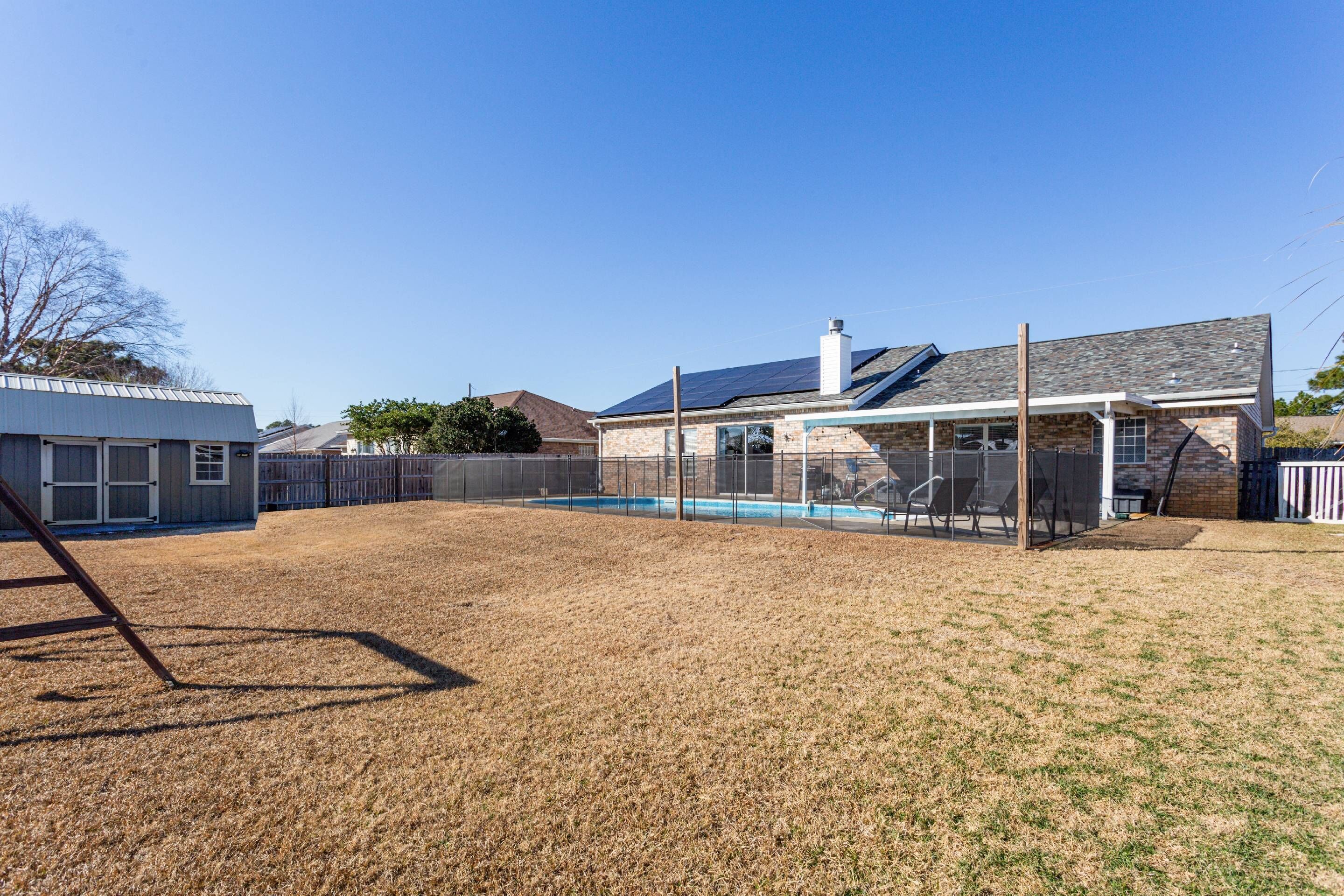 A backyard with a fenced pool, a covered patio, and a house with a sloped roof.