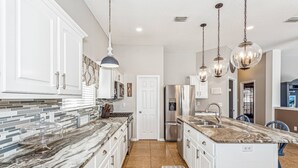 A modern kitchen with white cabinets, a marble countertop, and stainless steel appliances.