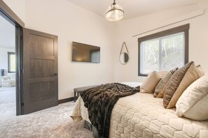Ein Schlafzimmer mit Bett, großem Fenster, Tür, Spiegel und Deckenleuchte.