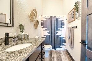 Ein Badezimmer mit Marmorwaschtisch, Toilette und Dusche mit geometrischem Duschvorhang.