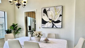 Un comedor con una mesa dispuesta para cuatro personas, una araña, un cuadro y una planta en maceta.