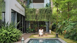 Un edificio moderno con facciata in vetro, area piscina e vegetazione lussureggiante.