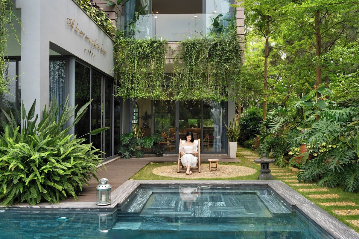 A modern building with a glass facade, a pool area, and lush greenery.