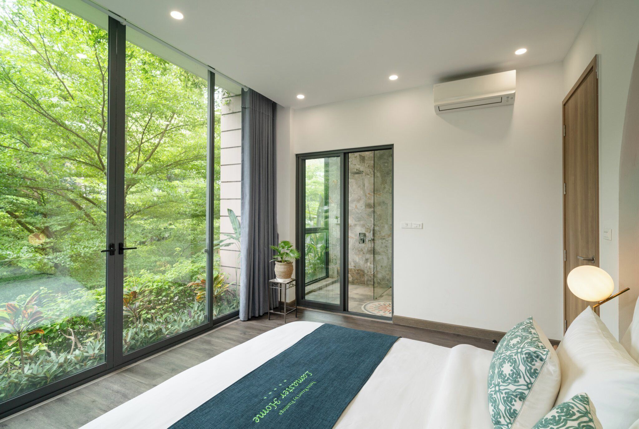 Un dormitorio moderno con un ventanal grande, una cama con un corredor verde y una puerta corrediza de vidrio que da a un balcón.