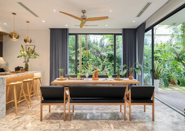 A modern dining area with a wooden table, black cushioned benches, and a ceiling fan. - Lamaster Homes F1.8 Venus Resort (Phuc Yen)