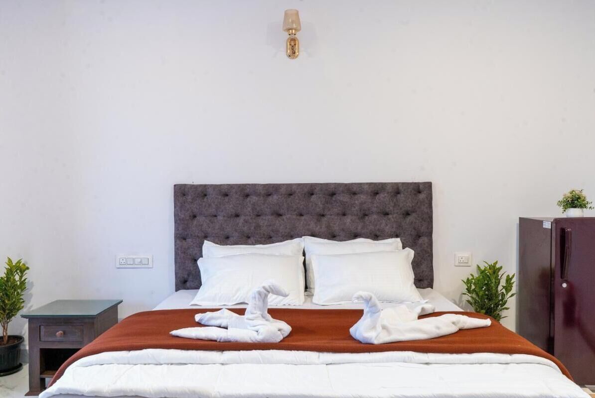 A neatly made bed with white linens, a grey tufted headboard, and two white towels folded on the bed.