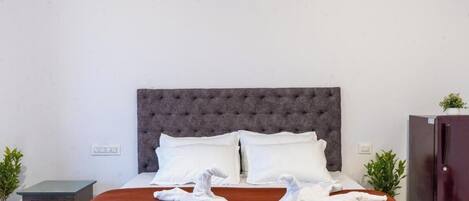 A neatly made bed with white linens, a grey tufted headboard, and two white towels folded on the bed.