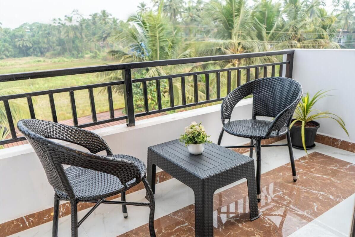 A balcony with wicker chairs and a small table, a potted plant, and a view of a green landscape.