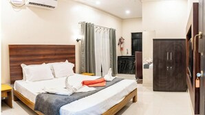 A hotel room with a wooden bed, a small bedside table, an air conditioning unit, a wardrobe, and a bathroom with a shower curtain. - Artham Guesthouse (Morjim)