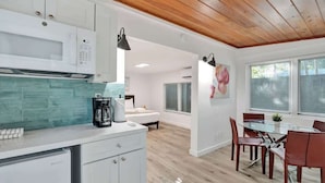 A modern kitchen with white cabinets, a microwave, and a coffee maker. There is a dining area with a glass table and red chairs. - Tropical Studio + Pool | Riverside Ft Lauderdale (Fort Lauderdale)