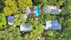 Vue aérienne d’un complexe hôtelier doté d’une piscine entourée d’une végétation luxuriante, de deux grands bâtiments et d’un espace aménagé avec des chaises longues.