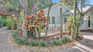 Une maison dotée d’un porche, entourée de plantes et d’arbres tropicaux.
