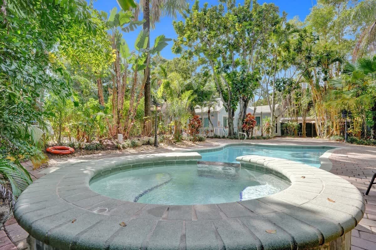 A hot tub surrounded by lush tropical vegetation and a clear pool.