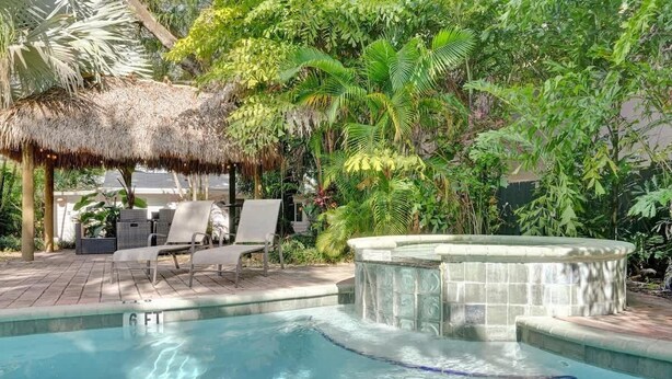 Un espace piscine doté de chaises longues, d’un jacuzzi et d’une végétation tropicale luxuriante.