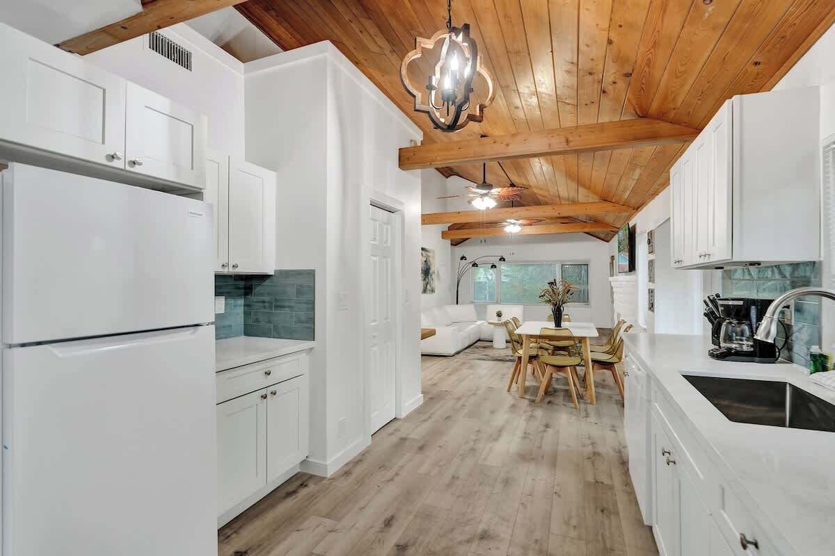 A modern kitchen with white cabinetry, a wooden ceiling, and a dining area with a table and chairs.