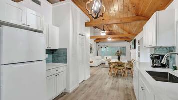 A modern kitchen with white cabinetry, a wooden ceiling, and a dining area with a table and chairs.