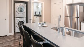 A modern kitchen with a stainless steel refrigerator, a built-in washing machine, and a bar area with chairs.