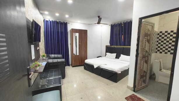 A compact hotel room with a bed, a desk, a chair, a TV, and a bathroom visible through an open door. - HOTEL VCR INN (New Delhi)