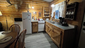A rustic kitchen with wooden walls, a white refrigerator, a stove, and a sink.
